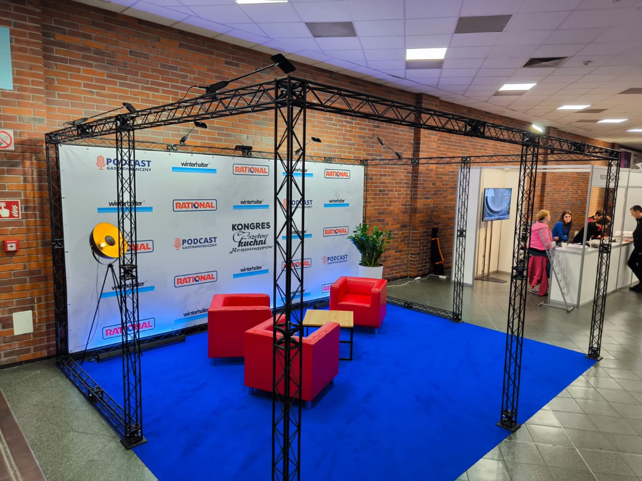 Stoisko eventowe z niebieską wykładziną i konstrukcją kratownicową